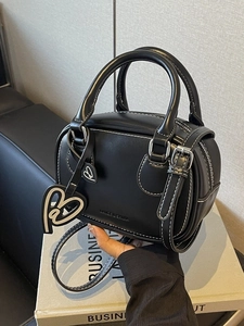 Black mini bowling handbag with white contrast stitching and heart charms on a desk