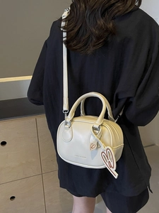 Chic cream bowling bag with top handles, crossbody strap and heart charm detail