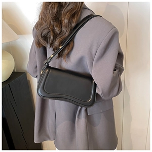 Detail view of the black leather underarm bag with gold hardware worn by a model