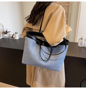 Detail of light blue denim tote bag with black leather trim worn by model in trench coat