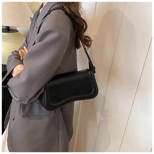 Detail view of the sleek black leather underarm bag with curved bottom and thin shoulder strap
