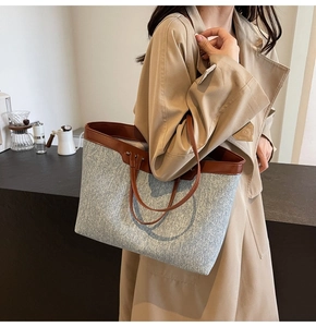 Detail of grey denim tote bag with brown leather handles worn over the shoulder