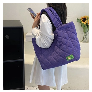 Close-up of purple quilted tote bag featuring a green woven label and ruched shoulder strap