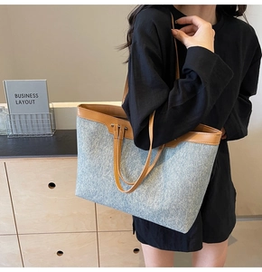 Close-up of light blue denim tote bag with brown leather handles and rivet details