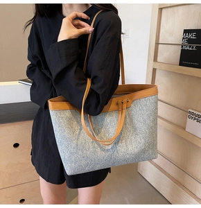 Model carrying a large denim and leather tote bag in a modern minimalist setting