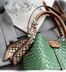 Detail of dark green woven bucket bag with brown leather handle and patterned silk scarf decor