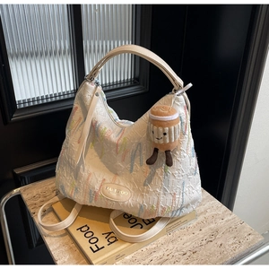 Detail of white embroidered hobo bag with colorful patterns and coffee cup plush charm