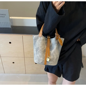 Detail of grey textured bucket bag with brown leather handles and orange charm
