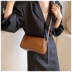 Detail of a brown minimalist crossbody bag with wave-shaped bottom and matte leather finish