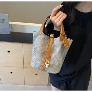 Detail of grey bucket bag with brown leather handles and gold lock charm on model