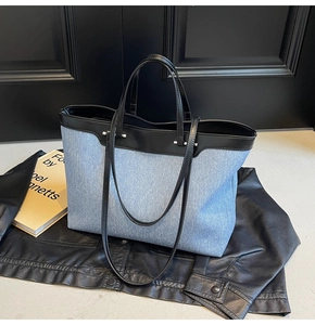 Detail of blue denim tote bag with black leather trim resting on a stylish leather jacket