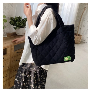 Quilted black corduroy tote bag with diamond stitching shown in a cozy home setting