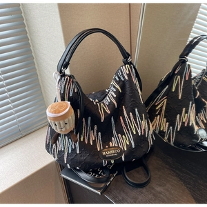 Detail of black pleated tote bag with letter embossing and colorful wave embroidery