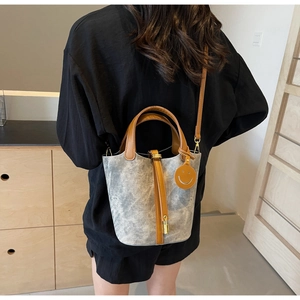 Detail of grey bucket bag with brown leather straps and yellow smiley charm on side