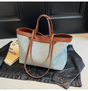 Detail of light blue denim and brown leather tote bag on a black jacket with book