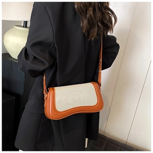 Detail of a chic orange leather and cream canvas underarm bag worn by a model