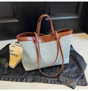 Blue denim tote bag with brown leather handles placed on a black jacket with a book