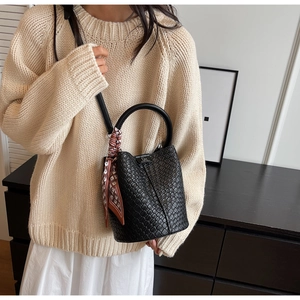 Detail of black woven bucket bag with elegant silk scarf and gold brand logo plate