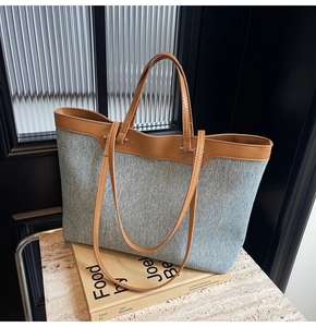 Detail of denim tote bag showing brown leather handles and silver metal hardware