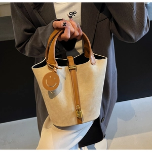 Detail of canvas bucket bag with brown leather trim and golden H-shaped metal lock