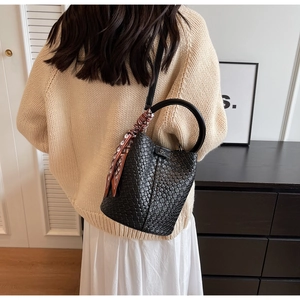 Detail of black woven bucket bag with metal logo and silk scarf on circular handle