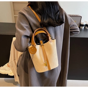 Detail of a beige canvas bucket bag with brown leather handles and a yellow smile tag
