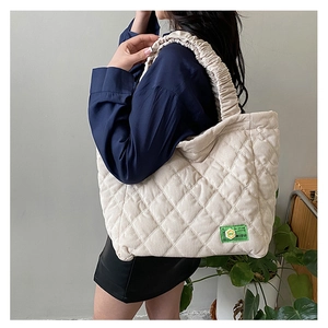 Detail of cream corduroy quilted tote with diamond stitching and pleated handle on a model