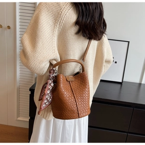 Close-up of brown woven bucket bag with patterned silk scarf on handle and metal logo
