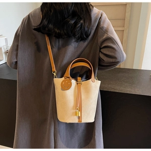 Canvas bucket bag with leather trim and gold padlock shown worn with a grey coat