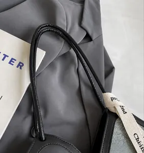 Détail de la fine bandoulière en cuir noir et du ruban en toile lettré sur le sac fourre-tout