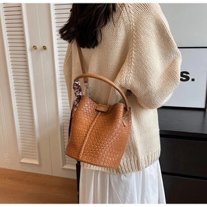 Detail of a brown woven leather bucket bag with a decorative floral silk scarf on the handle