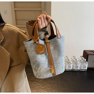 Detail of denim bucket bag featuring leather handles and a smile charm with gold padlock