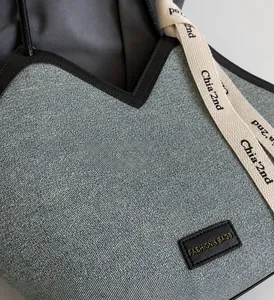 Détail d'un sac cabas en denim bleu avec garniture en cuir et bandoulière tissée