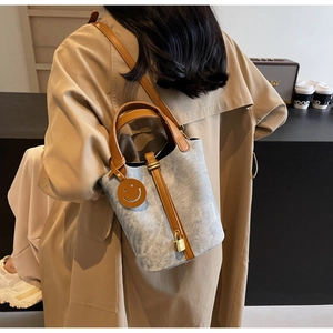 Detail of blue bucket bag with leather straps and gold lock on a trench coat background