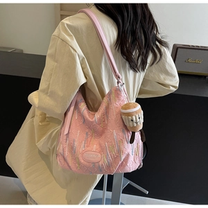 Pink textured hobo bag with colorful embroidery and a plush charm in a lifestyle setting