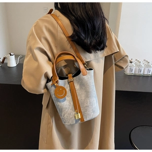 Detail of grey bucket bag with brown leather straps, gold lock, and smiley pendant