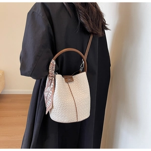 Detail of a creamy white bucket bag with crocodile texture and silk scarf decoration