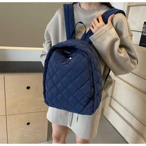 Detail eines dunkelblauen gesteppten Rucksacks mit glänzendem Rautenmuster und Stickerei