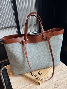 Large capacity denim tote bag with brown leather handles on marble countertop