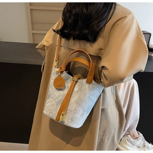 Detail of light blue denim bucket bag featuring leather handles and gold padlock charm