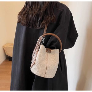 Detail view of cream bucket bag with crocodile texture, round handle, and floral silk scarf