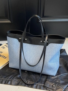 Large denim tote bag with black leather straps on dark leather background