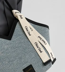 Détail du sac cabas en denim avec bandoulière tissée décorative et bordure en cuir noir