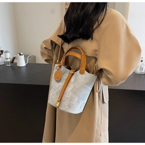 Detail of light blue denim bucket bag with brown leather handles and gold lock charm