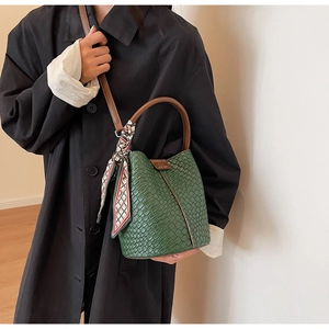 Detail of dark green woven bucket bag featuring a silk scarf handle and logo accent