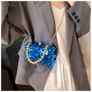 Detail view of a blue transparent bubble handbag with golden beads and a fine metal chain strap