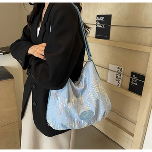 Detailed shot of light blue shoulder bag featuring colorful wavy embroidery and pleated texture