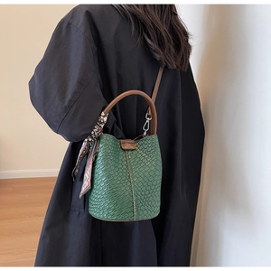 Detail of green textured bucket bag with silk scarf and brown top handle over black coat