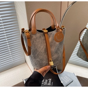 Detail of grey bucket bag showing leather handles, gold lock and smiley charm accent