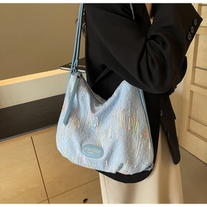 Detail showing colorful wavy embroidery and leather brand logo on a light blue shoulder bag
